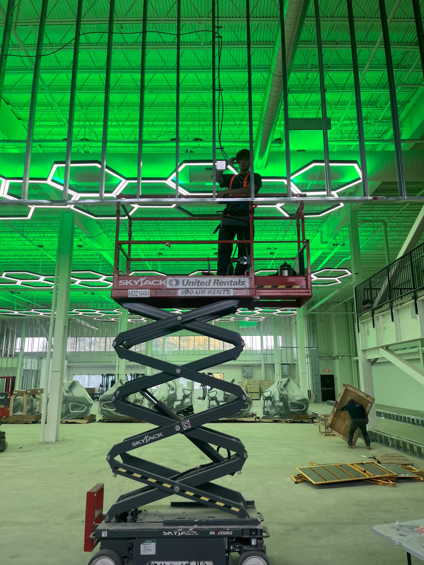 Electron Services electrician on a scissor lift installing hexagon LED grid lighting in a fitness facility